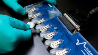 A person's hand is shown inserting a coin battery into a testing device.