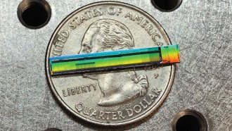 A rainbow-hued strip with black markings on it sits atop a U.S. quarter