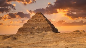 Egyptian King Djoser's pyramid rises above a sandy landscape, while sun-tinged clouds cast a golden glow on the scene.