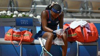 A tennis player sitting on a bench, holding a bag of ice to cool down from the heat during the 2024 Olympics in Paris.