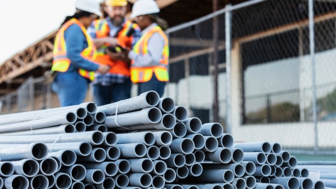 A stack of PVC pipe lies in front of workers.