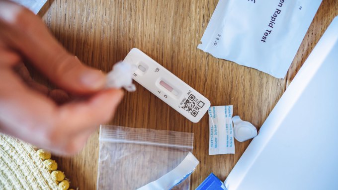 A photo of a COVID-19 test kit and a person using the test.